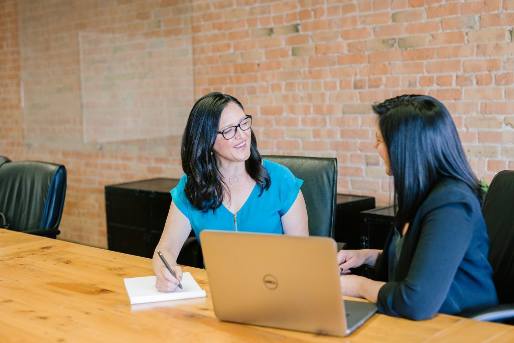 woman in teal t-shirt sitting beside woman in suit jacket talking