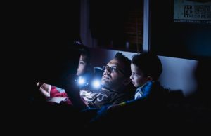 man in blue shirt lying on bed reading a story to kids