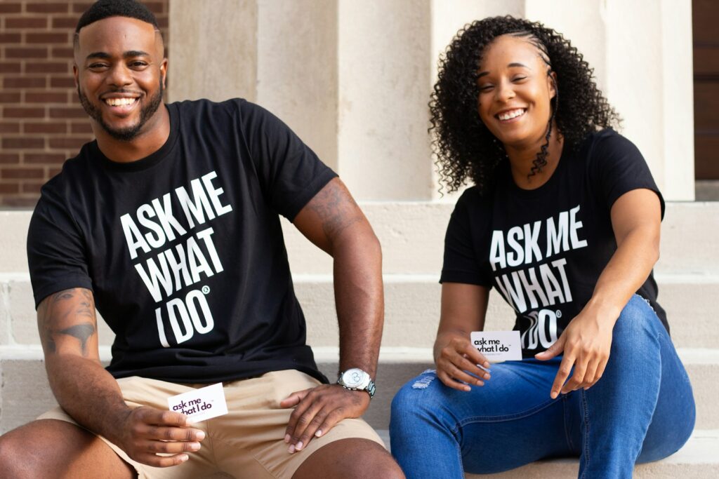 man in black crew neck t-shirt sitting beside woman in blue denim jeans with a t-shirt that says "Ask me what I do"